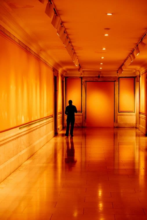 A person walks down a dimly lit corridor with orange walls and reflective flooring, creating a warm, serene atmosphere.