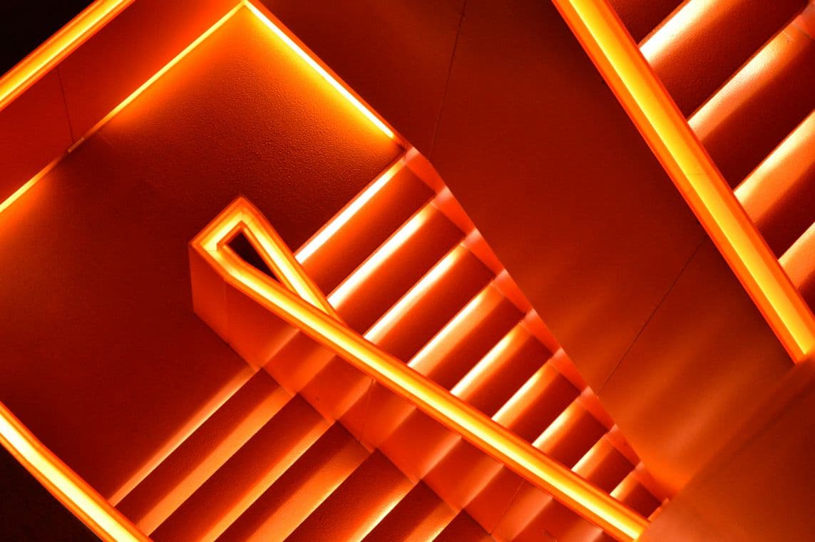 A spiral staircase with glowing orange LED lights along the edges, creating a vibrant, futuristic appearance against a dark background.
